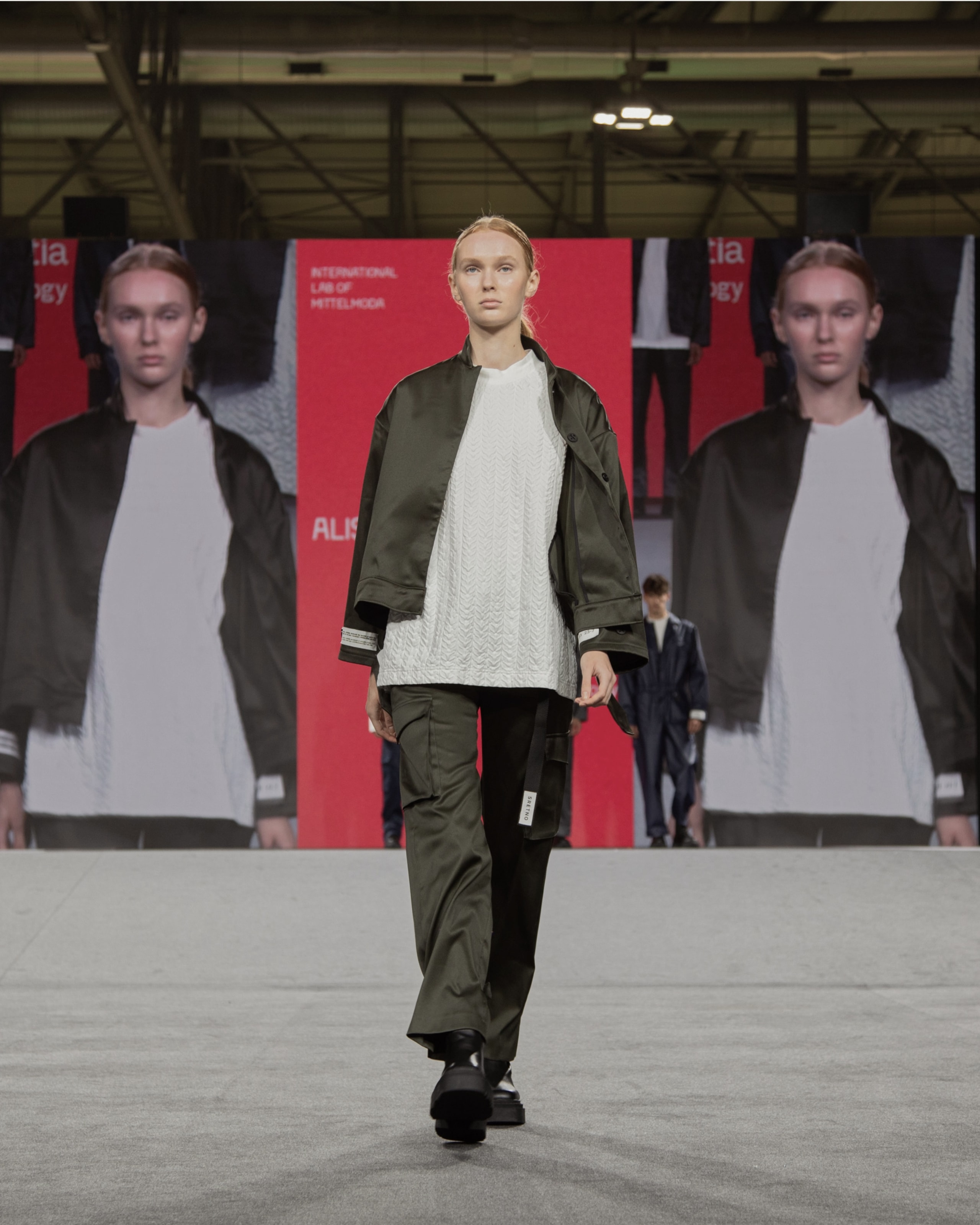 Model wearing green jacket, pants, and white t-shirt from KOVARI collection on Mittelmoda show.