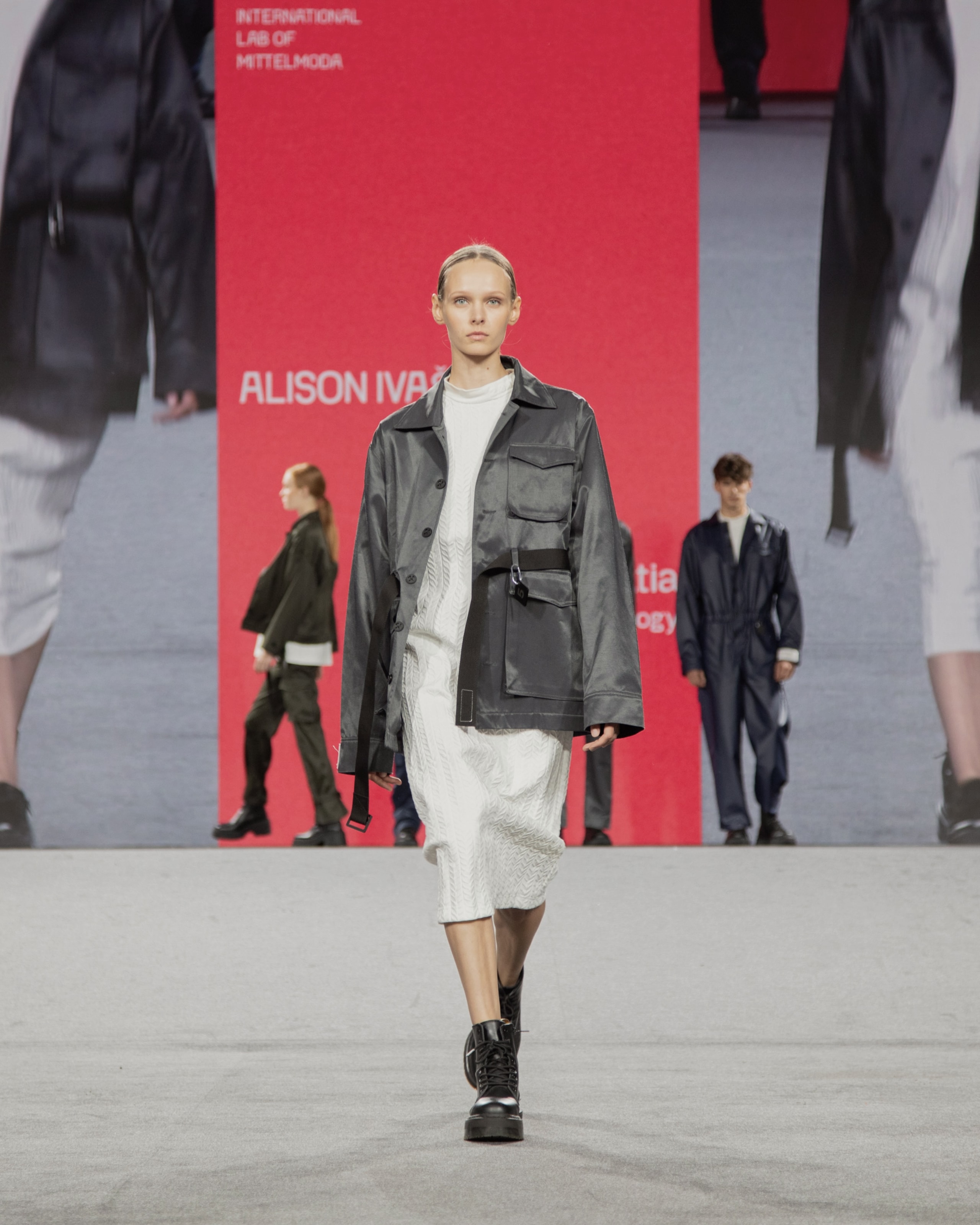 Model wearing gray jacket and white dress from KOVARI collection on Mittelmoda show.