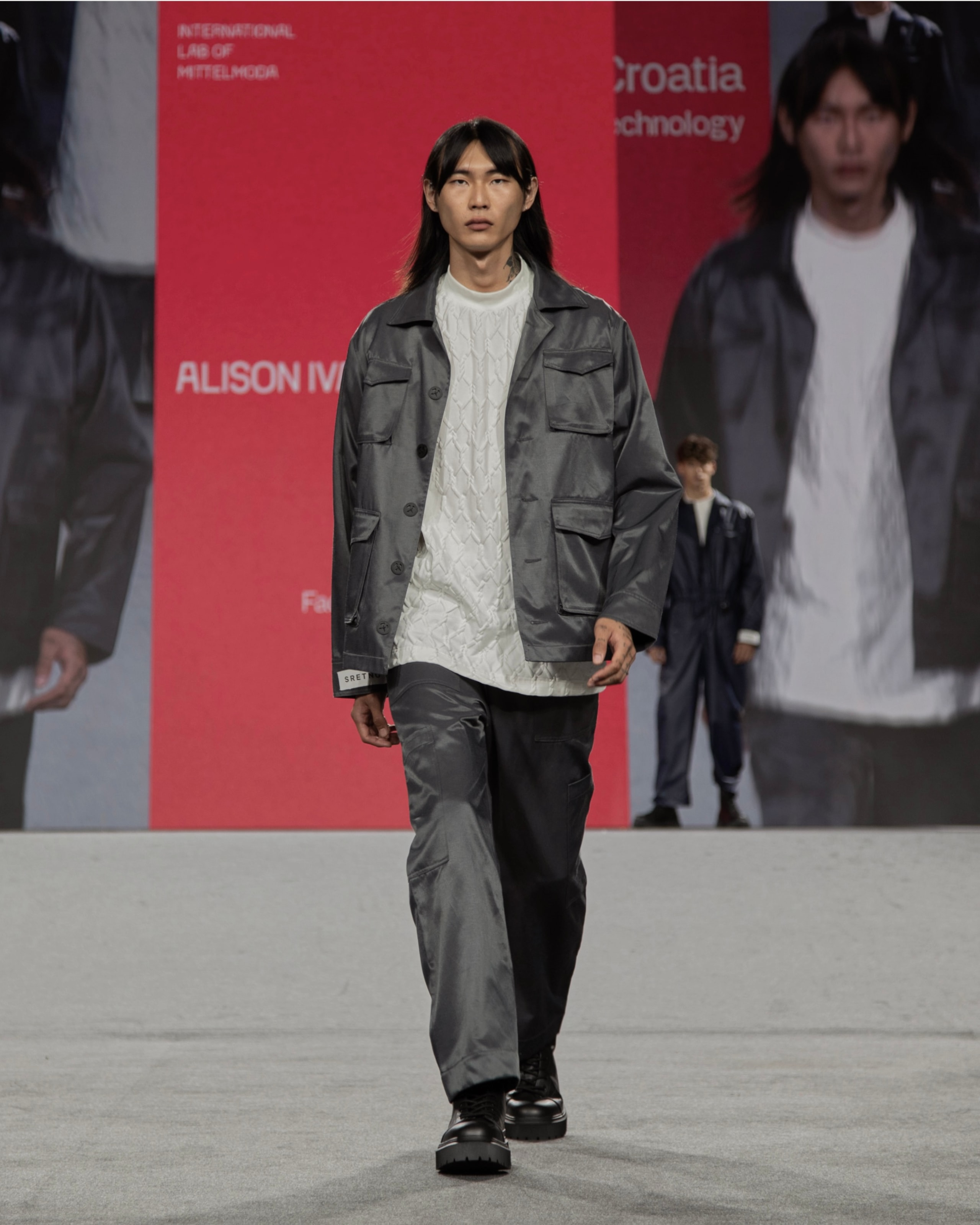 Model wearing grey jacket, pants, and white t-shirt from KOVARI collection on Mittelmoda show.