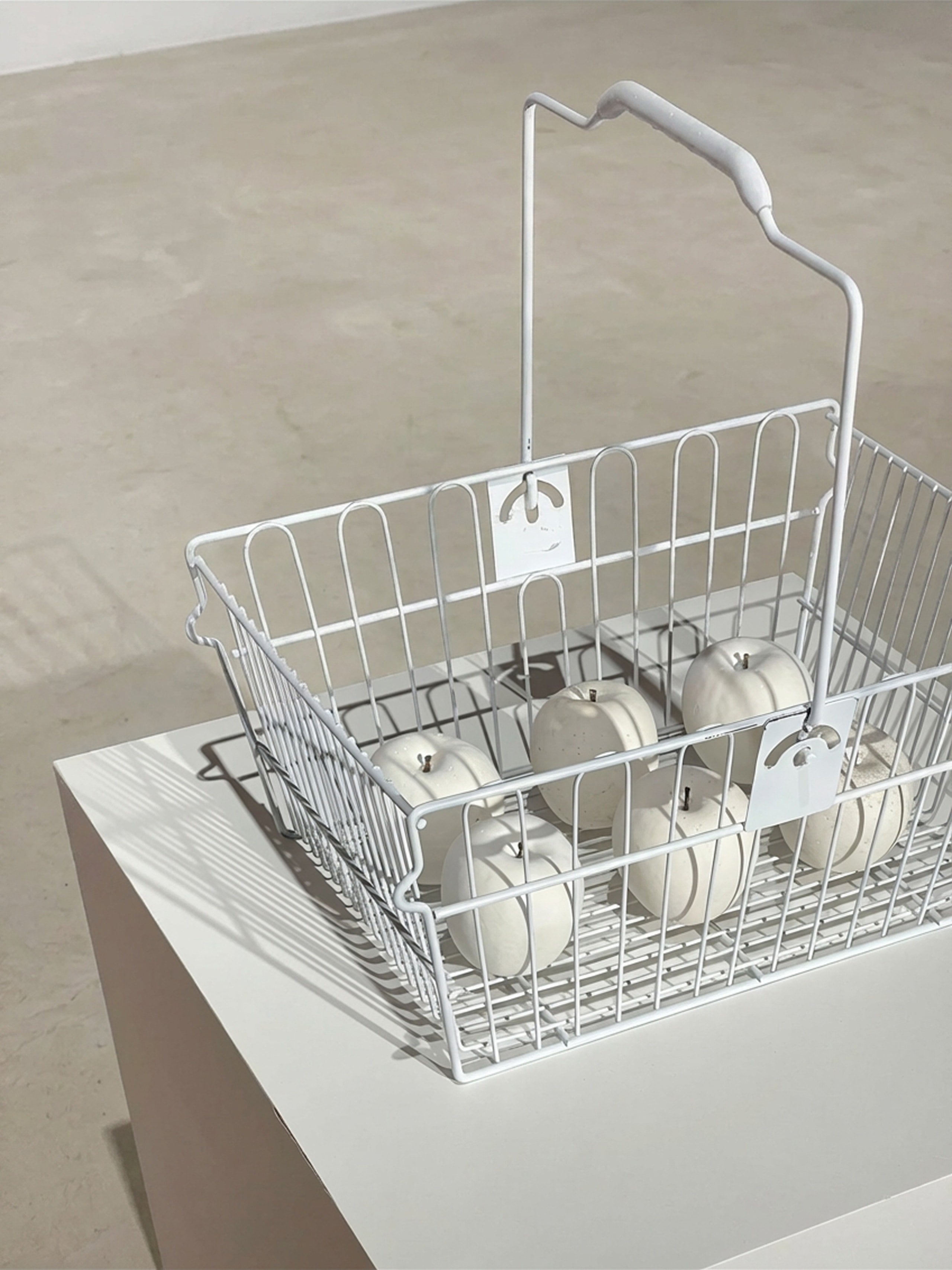 Sculpture that is made of six white plaster apples and white metal shopping cart. 